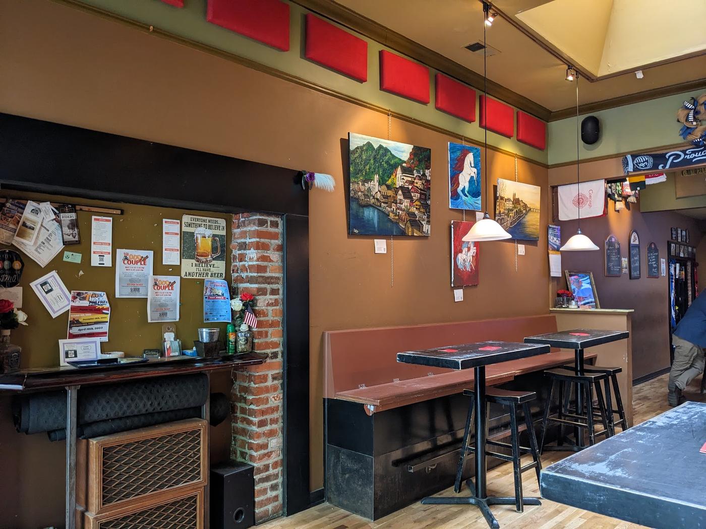 Inside Gumbo Bottoms: original paintings hung on the wall with price cards beneath them, a community noticeboard and high tables